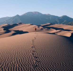 person walking on sand dunes leaving footprint trails behind photo