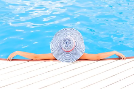 woman leaning on white concrete surface beside swimming pool during daytime photo