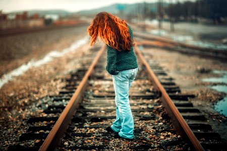 woman with orange hair wearing black and gray stripe long-sleeve shirt and light-blue denim pants standing on train rail at day photo