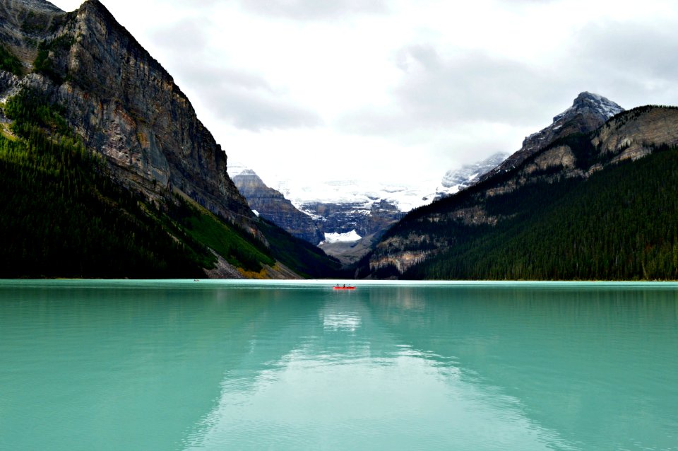 person riding on canoe boat in between hill on body of water