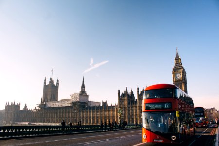 red double-decker bus passing Palace of Westminster, London during daytime photo