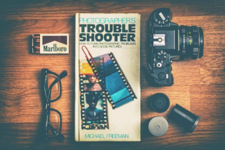 Photographers Trouble Shooter book between DSLR camera, Marlboro match box and eyeglasses photo