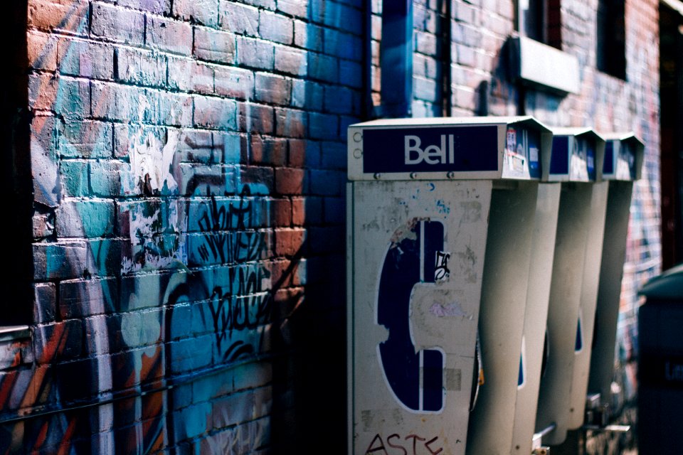 white and black Bell phone booth beisde concrete bricked wall with graffiti