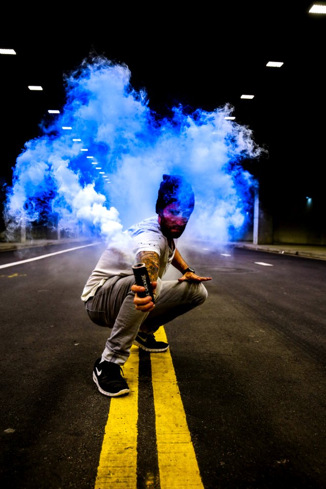 man holding black tube with blue smoke in the middle of road