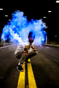 man holding black tube with blue smoke in the middle of road