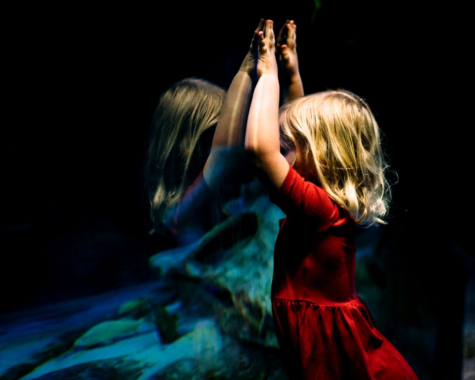 girl leaning on glass fish tank raising her two hands