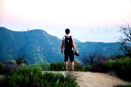 man wearing black backpack standing near mountain at daytime