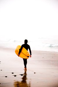 man holding yellow surfboard while walking on seashore during daytime photo