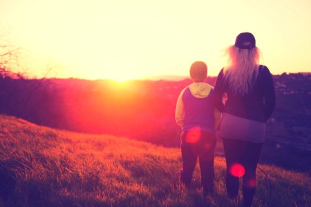 silhouette photo of woman standing beside a child on grass field