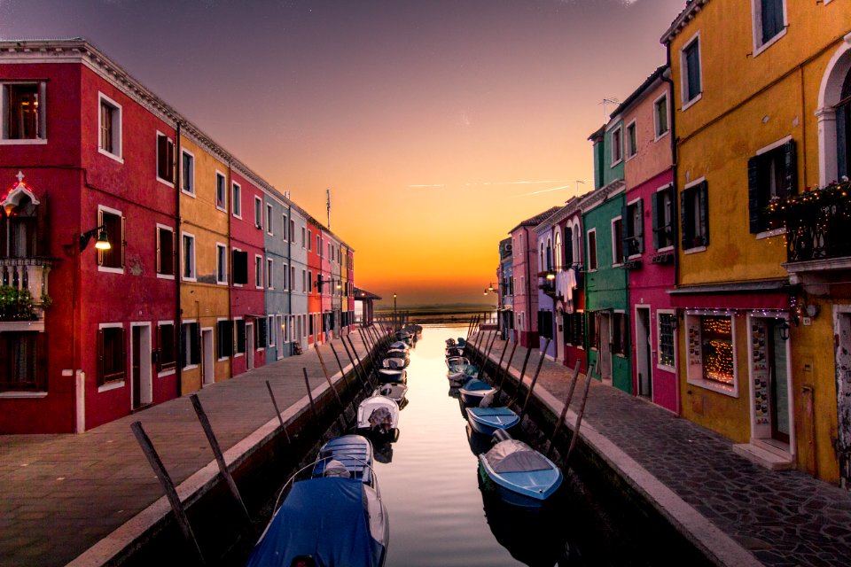 blue boats parked on river between multicolored buildings at sunset