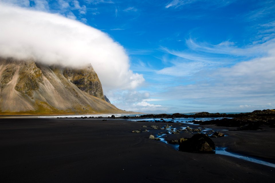 mountain hill covered with clouds near body of water during daytime