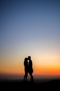 Two people kiss silhouetted against a sunset sky photo