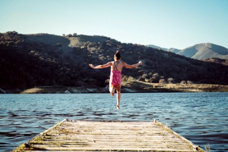 woman wearing pink top jumping towards water during daytime photo