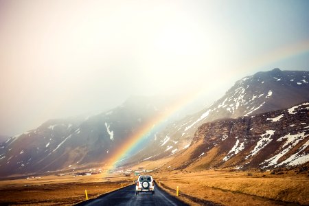 white car travelling near mountains with rainbow photo
