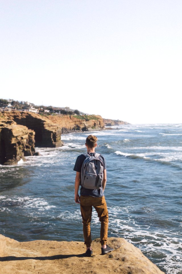 man standing on cliff looking at body of water