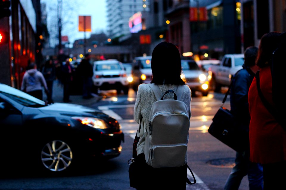 woman wearing grey shirt and white backpack facing car on street