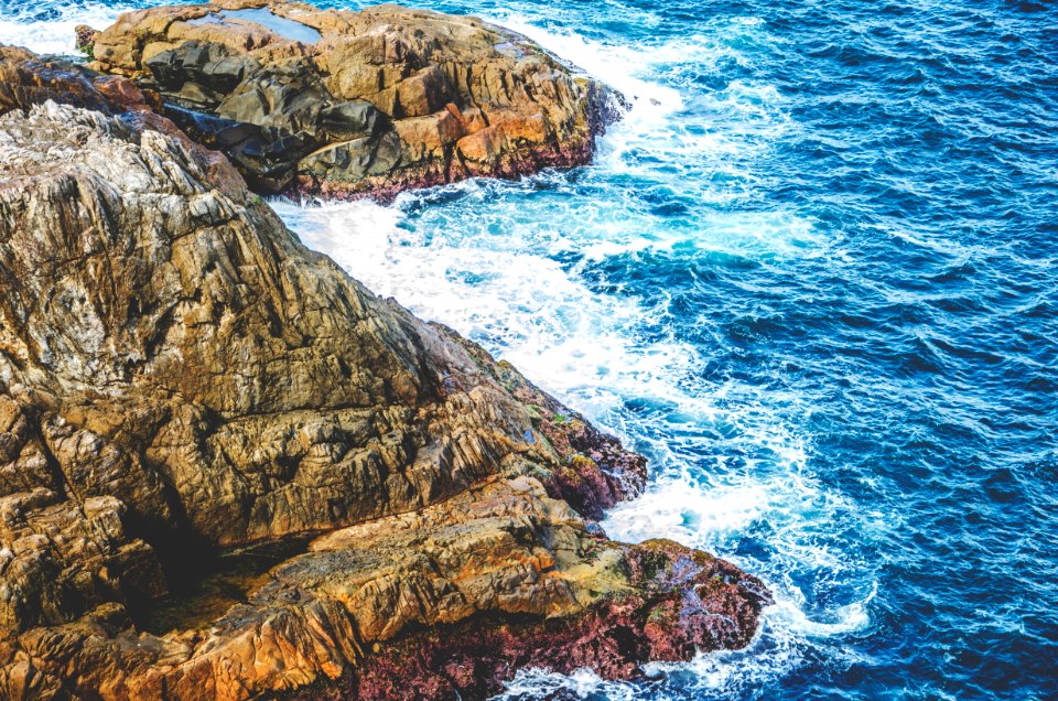 aerial photo of sea waves splashing through rocky mountain