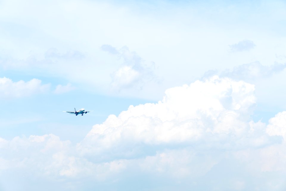 photo of white commercial airplane flying in sky under white clouds