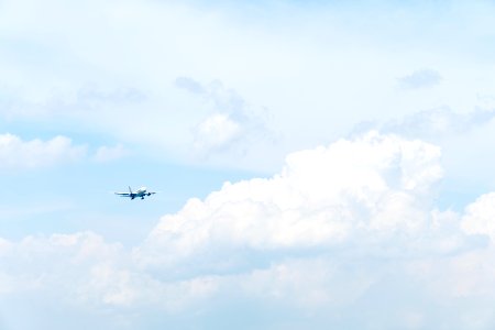 photo of white commercial airplane flying in sky under white clouds