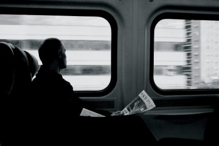 man inside train looking on window while holding newspaper grayscale photography photo