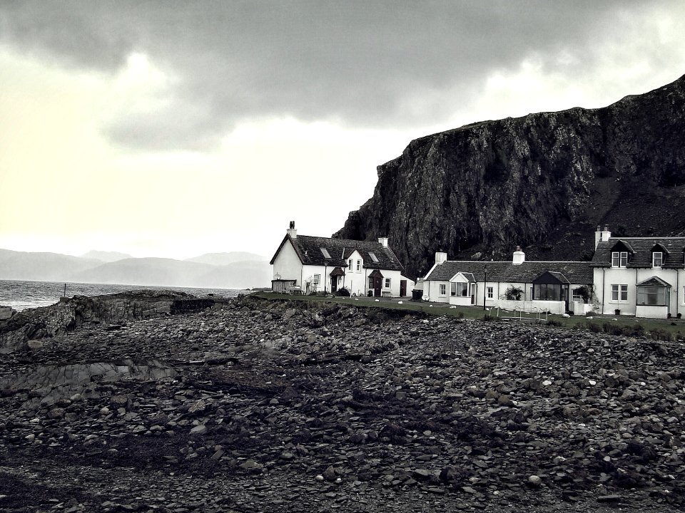 grayscale photography of houses near rocky mountain and body of water
