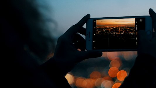 person capturing photo of city using iPhone during orange sunset photo