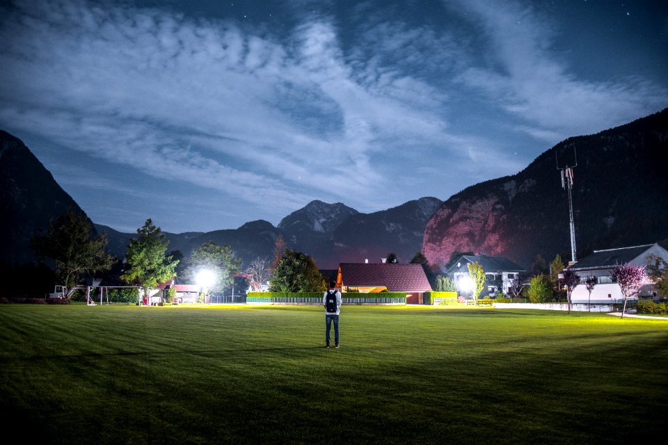 man in white shirt with black backpack standing on green grass field