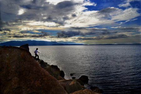 person standing on rocky cliff near body of water photo