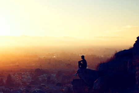 man sitting on rock formation in cliff during golden hours photo