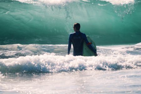 man standing in body of water holding surfboard photo