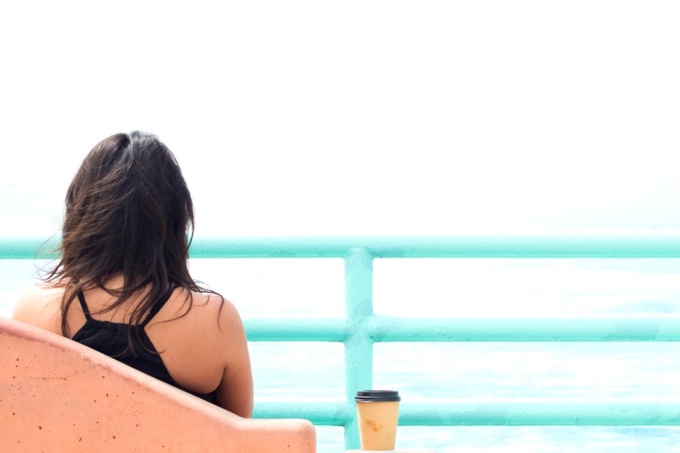 woman sitting on chair beside cup in front of body of water