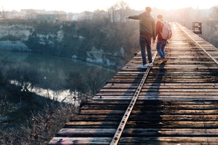 two boy standing on brown train track bridge near river photo