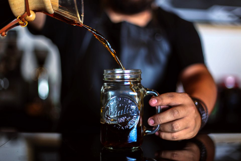 man pouring liquid on clear glass mason jar