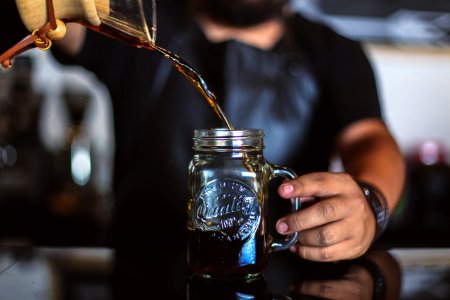 man pouring liquid on clear glass mason jar photo