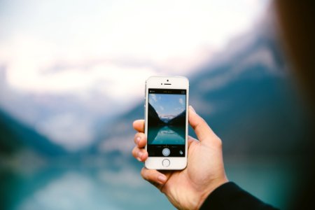 person holing silver iPhone 5s taking photo of body of water near mountains at daytime photo