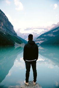 man standing in the middle rock facing lake photo