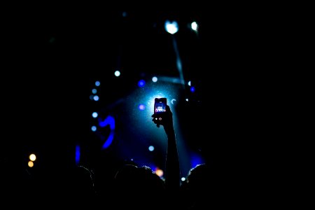 low light photography of person raising hand holding smartphone photo