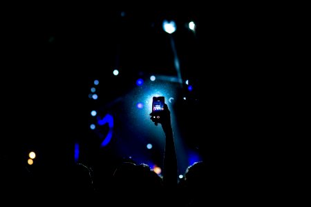 low light photography of person raising hand holding smartphone