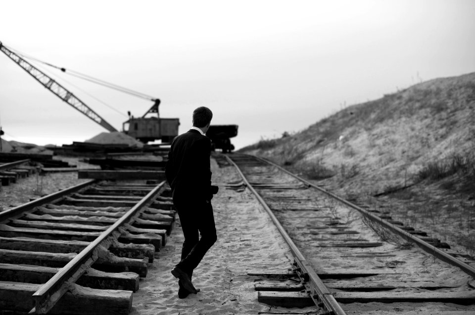grayscale of man walking on train rail