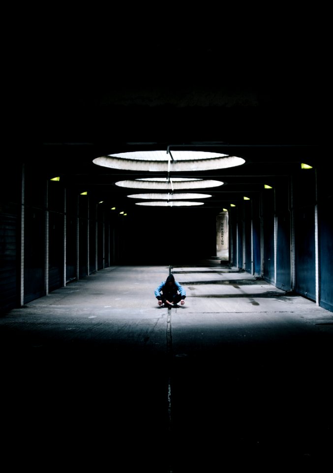 person sitting cross leg at hallway under glass ceiling between black wall