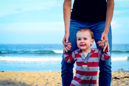 man assisting baby to walk on beach photo