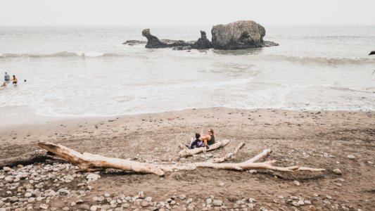 two men's sitting on shore near gray rock formation at daytime photo