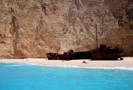 group of people on seashore near ship near mountain at daytime