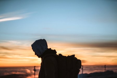 silhouette of person carrying backpack during orange sunset photo