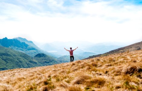 man topless standing on top of hill with dried grass field