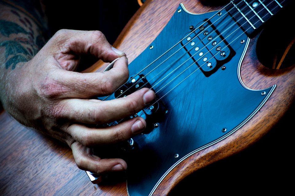 person plucking electric guitar with guitar pick