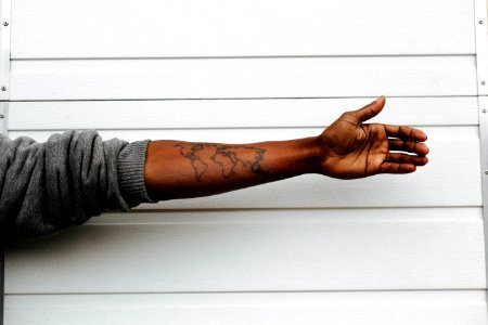 man raising hand with map arm tattoo behind white painted wall photo