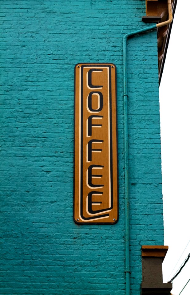 brown and black wooden coffee sign board on blue brick wall at daytime