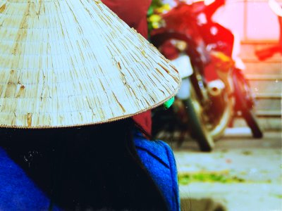 person wearing rice hat facing white motorcycle parked beside red wall photo
