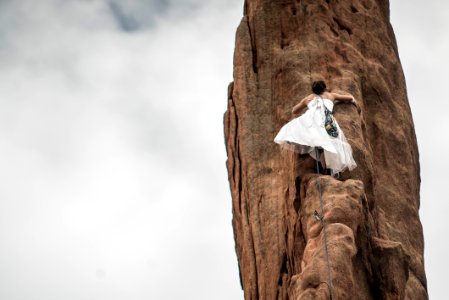 woman wearing white wedding dress climbing on brown rock under white sky photo